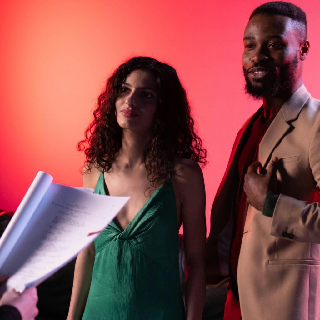 Actors discussing script during a studio shoot with dramatic lighting.